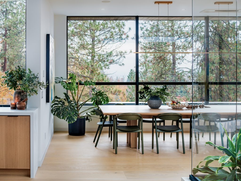 Dining area at the Crest project with full-height windows framing trees and a garden.