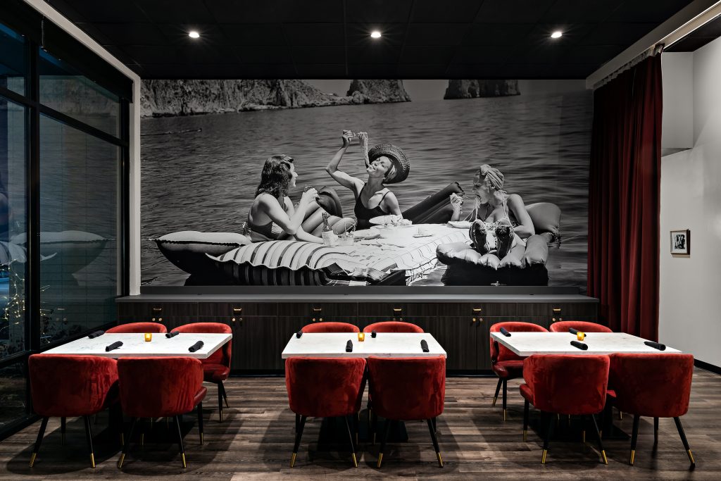 Enzo dining room with red upholstered seating, set tables, and a large monochrome wall mural.