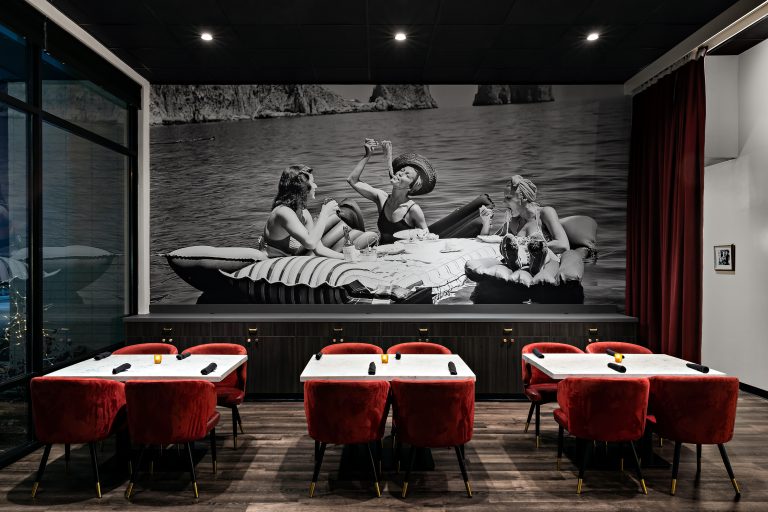 Enzo dining room with red upholstered seating, set tables, and a large monochrome wall mural.